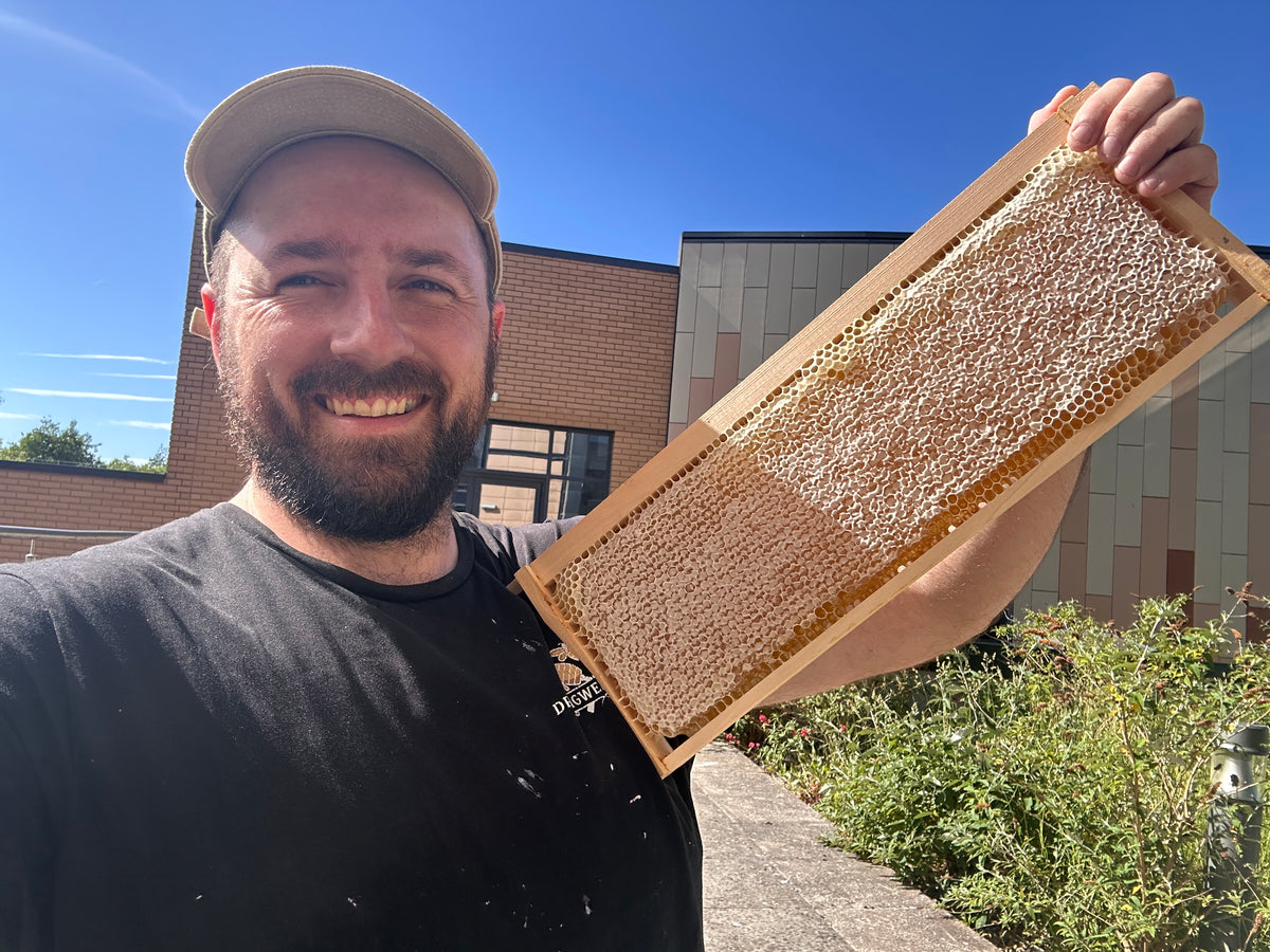 A man smiling and happy holding a full frame of honey with pride