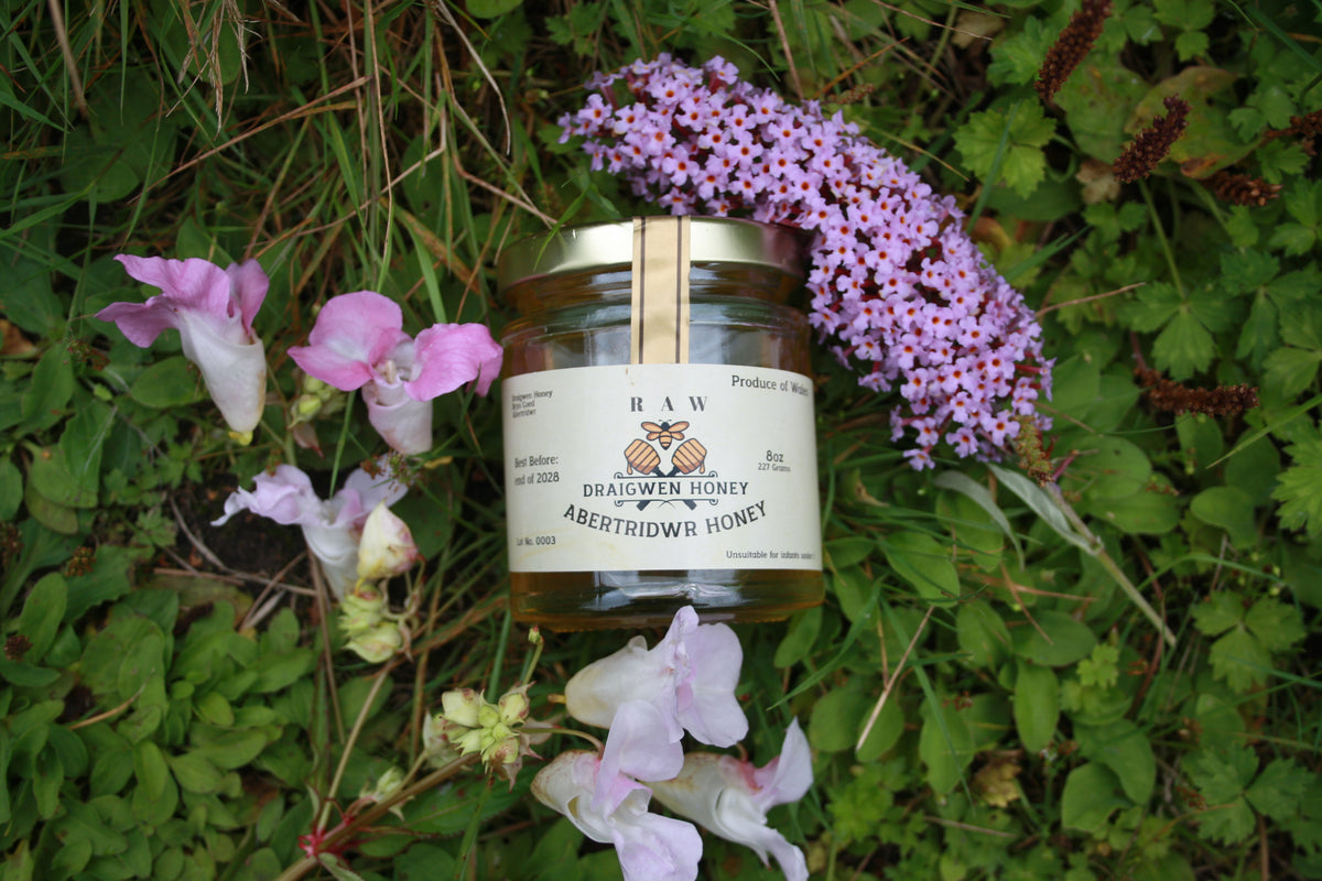 Jar of draigwen honey with a label on a grassy background with flowers