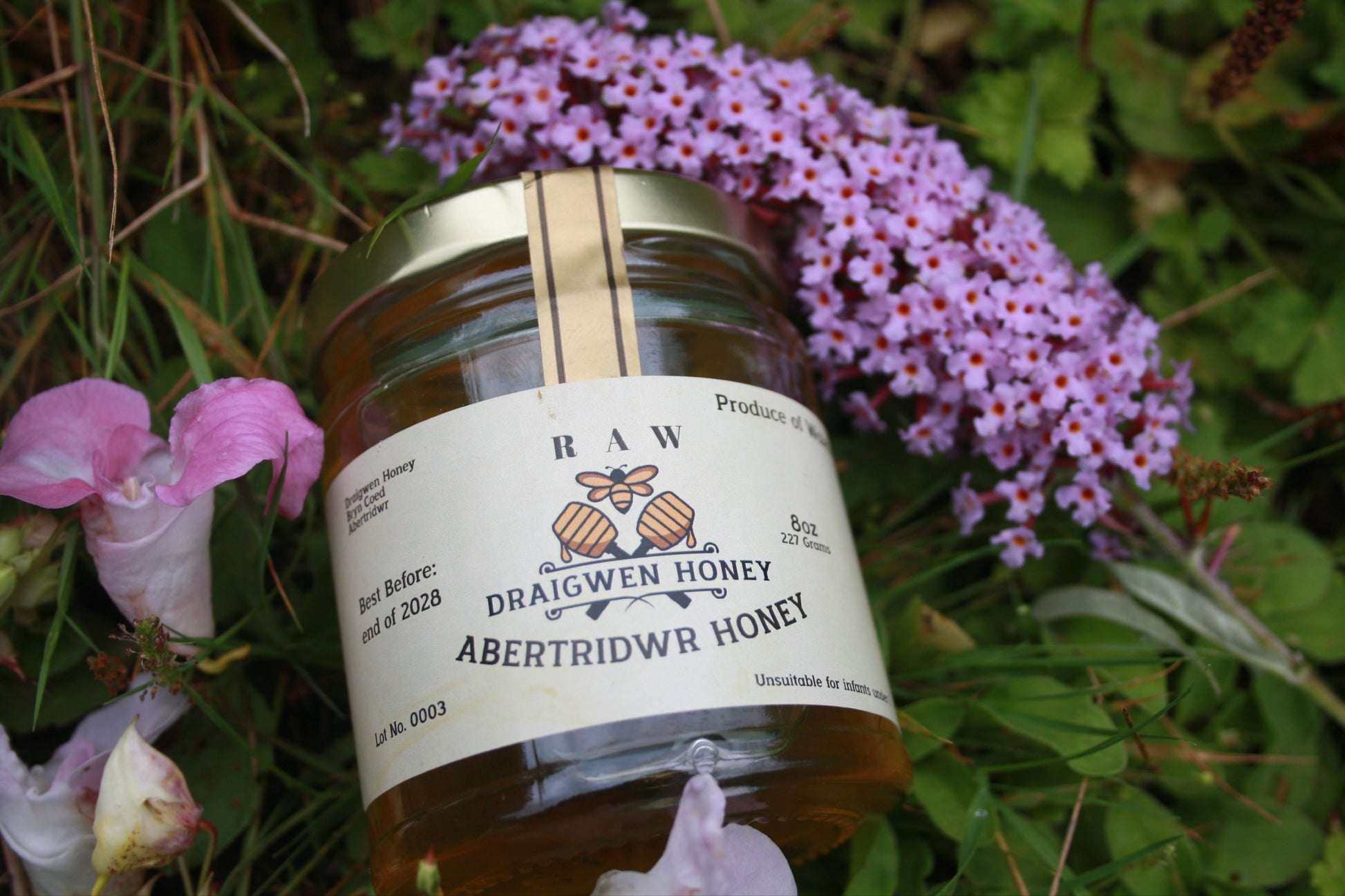 Jar of raw honey with a label on a grassy background with flowers