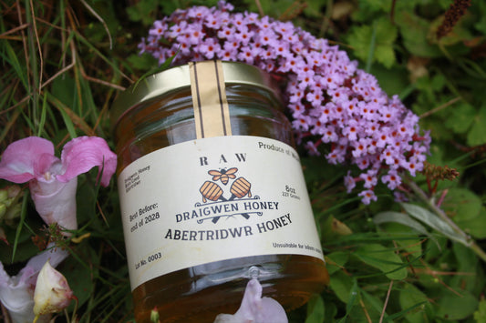 Jar of raw honey with a label on a grassy background with flowers